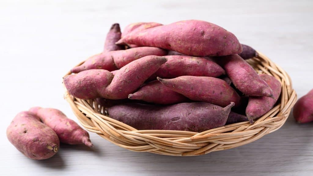 Batatas-doces orgânicas cruas em uma cesta sobre a mesa branca.