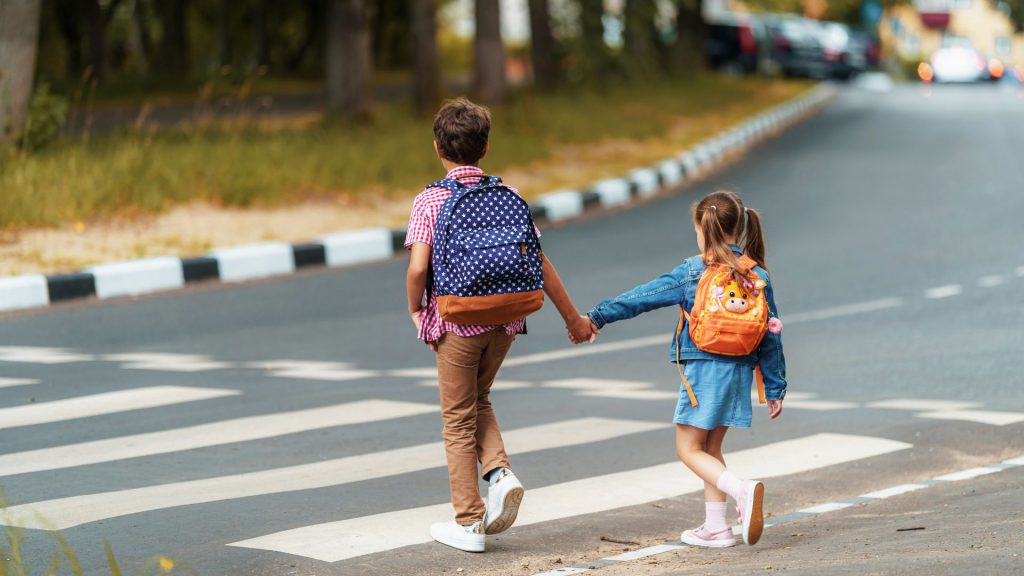 garota e menino com mochilas atravessam cuidadosamente a rua na faixa de pedestres a caminho da escola. Regras de trânsito. Caminho para pedestres ao longo da faixa zebrada na cidade. conceito de pedestres atravessando a faixa de pedestres.