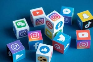 Imagem ilustrativa de cubos tridimensionais espalhados sobre um fundo azul, cada cubo possui em seus lados os logos de uma rede social