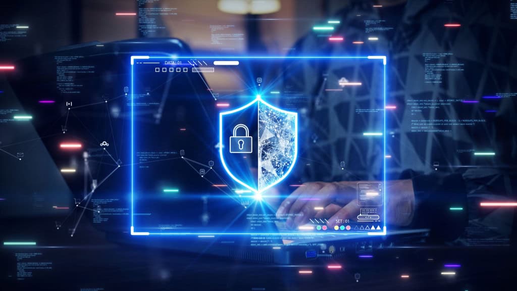 Montagem com ilustração digital de escudo de cibersegurança em cima de foto de pessoa digitando em computador