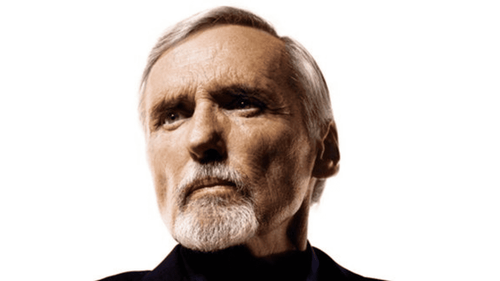 Dennis Hopper com expressão intensa e olhar fixo, retratado em ambiente escuro, em referência ao tema “atores que mais morreram em filmes e séries”
